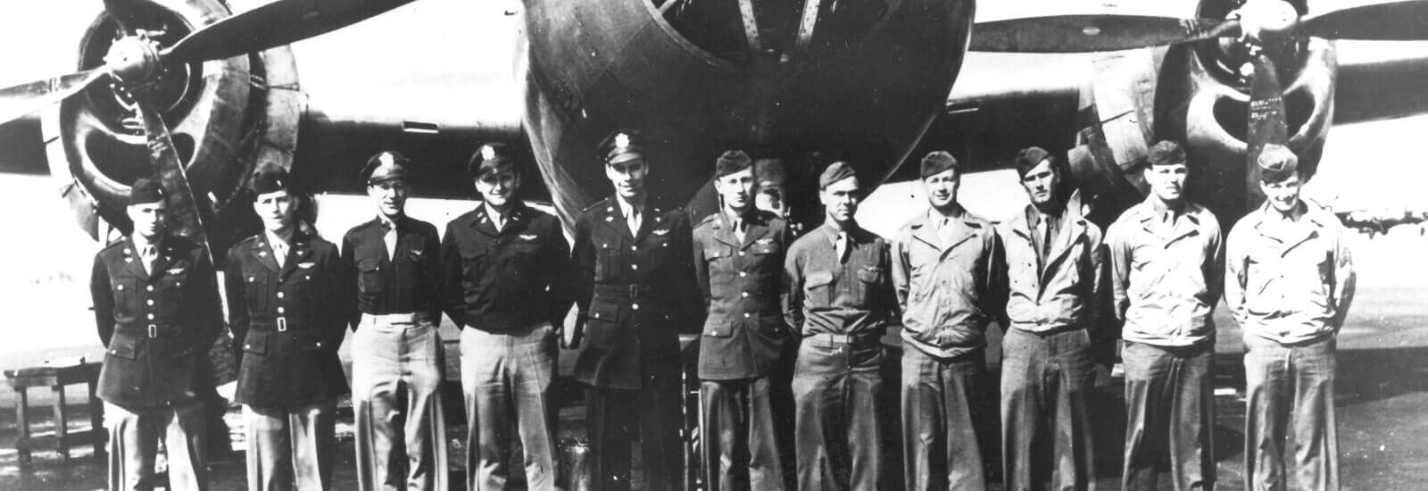 Old grayscale photo of WW2 soldiers standing in front of a bomber plane