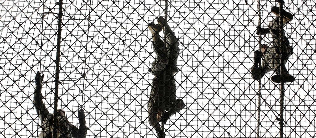 A group of soldiers climbing ropes in an obstacle course.