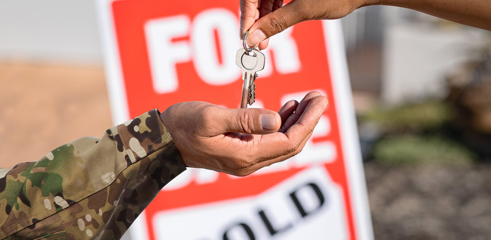 Image of a solider receiving house keys in front of a red "For Sale" sign