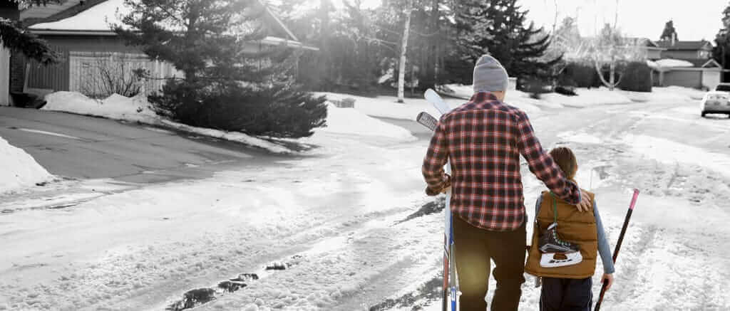 Dad and a child walking  with hockey skates down a street.