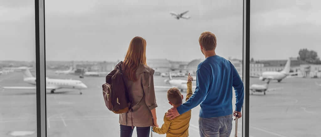 A Mom, Dad and child watching airplanes through the airport windows.