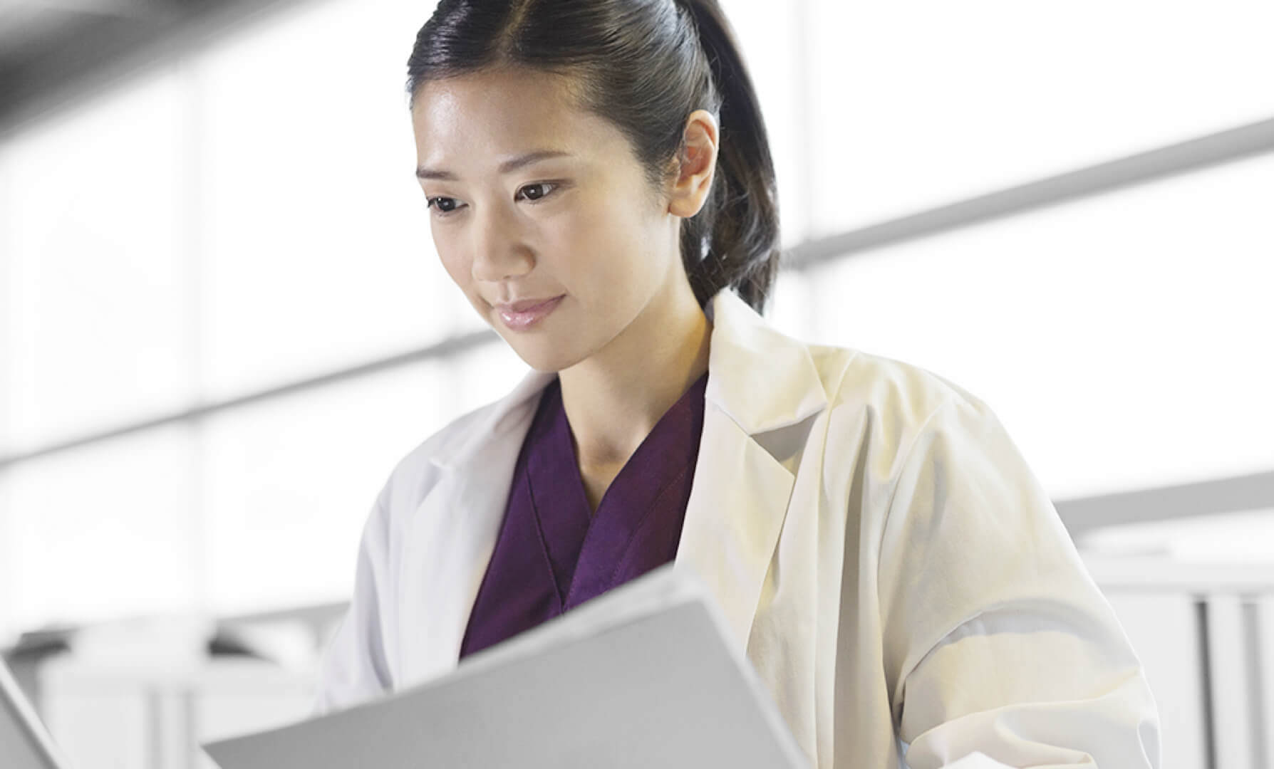 A woman in a white lab coat looking at a computer.