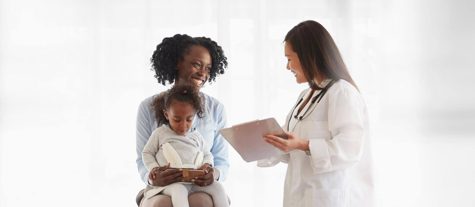 A mother speaking to a doctor while her daughter in her lap plays on cellphone.