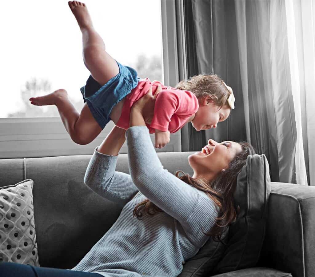 A woman playfully lifting a young child up and above her head.