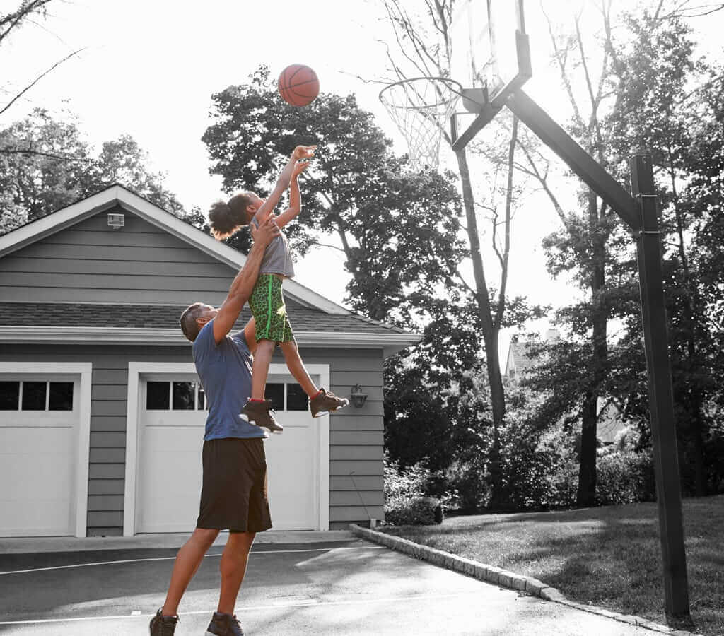 A Dad lifting his child up to shoot a basketball into the hoop.