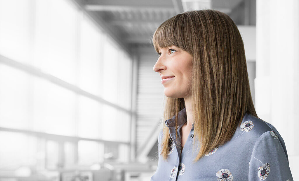 A woman in a floral shirt looking out a well lit office window