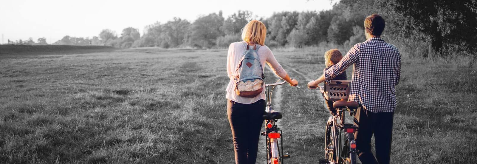 A family riding bikes with their young child through a grassy park