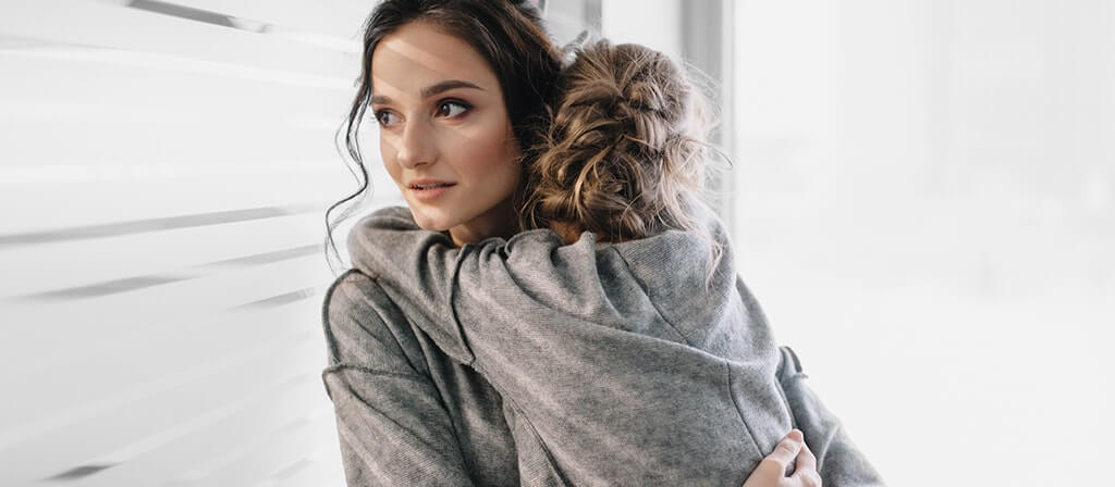 A woman is holding her baby and looking out through the window