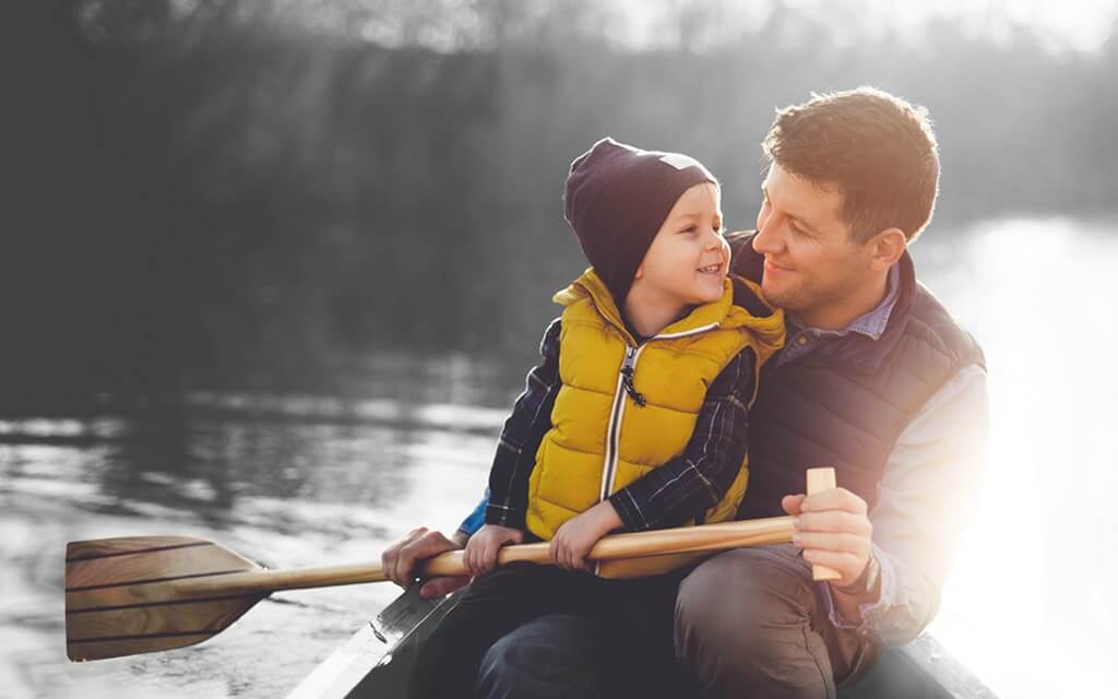 A father and his young son paddling in a canoe on a lake.